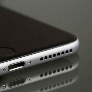 Home A sleek smartphone close-up highlighting its lightning connector and speaker, reflecting on a surface.